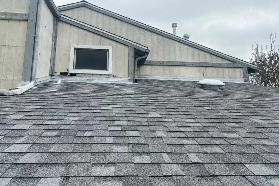 Daylight view of finished gray architectural shingles below a weathered wall.