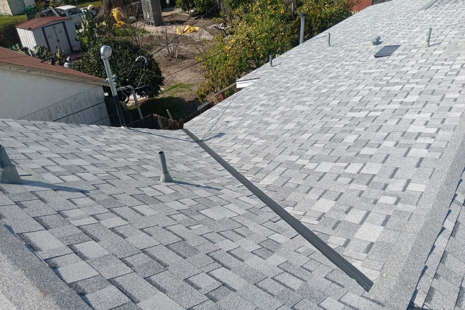 Daylight view of light-gray shingle planes with vents and a dark valley.