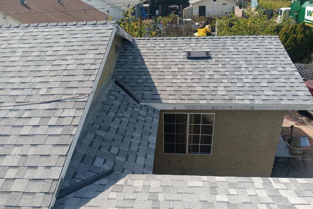 Roof-level photograph showing intersecting light-gray shingle roof planes.