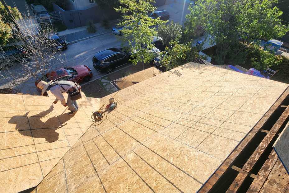Daylight view of roof deck sheathing during active installation.