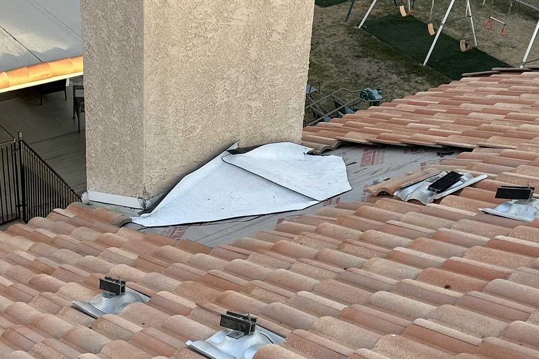 Roof-level photograph showing clay tile roofing around a chimney and metal flashing.
