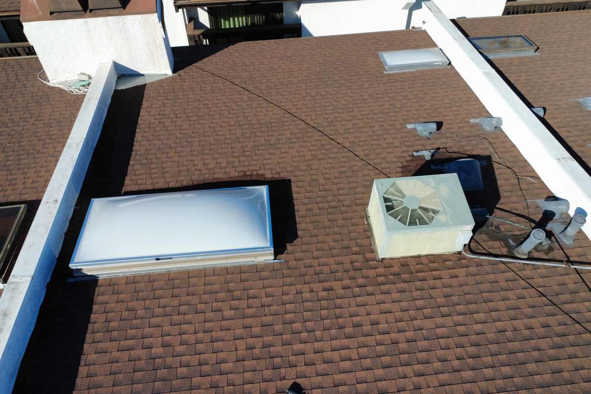 Roof-level photograph showing brown shingles adjoining pale low-slope roof sections.