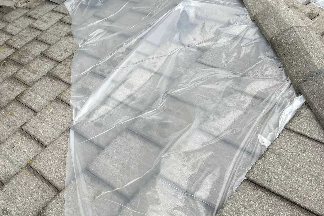 Daylight view of a clear protective sheet spread over a shingle roof.