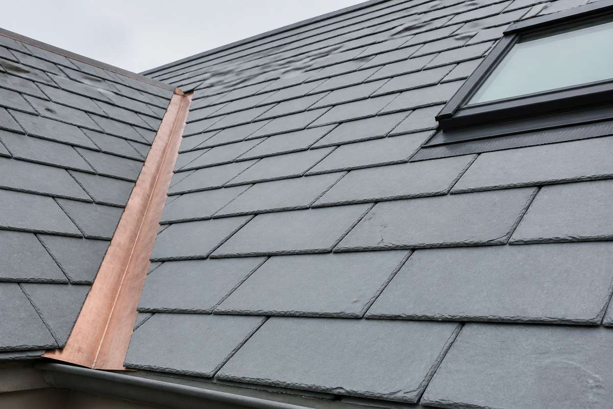 Daylight view of natural gray slate courses beside copper valley and roof-window flashing.